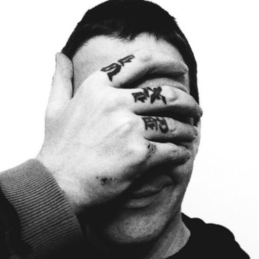 A black and white portrait of Christopher. He holds his right hand over his eyes, his knuckle tattoos are visible, and he is smirking. He has short hair and is wearing an Oakley hoodie. He looks to be twenty-seven years old.